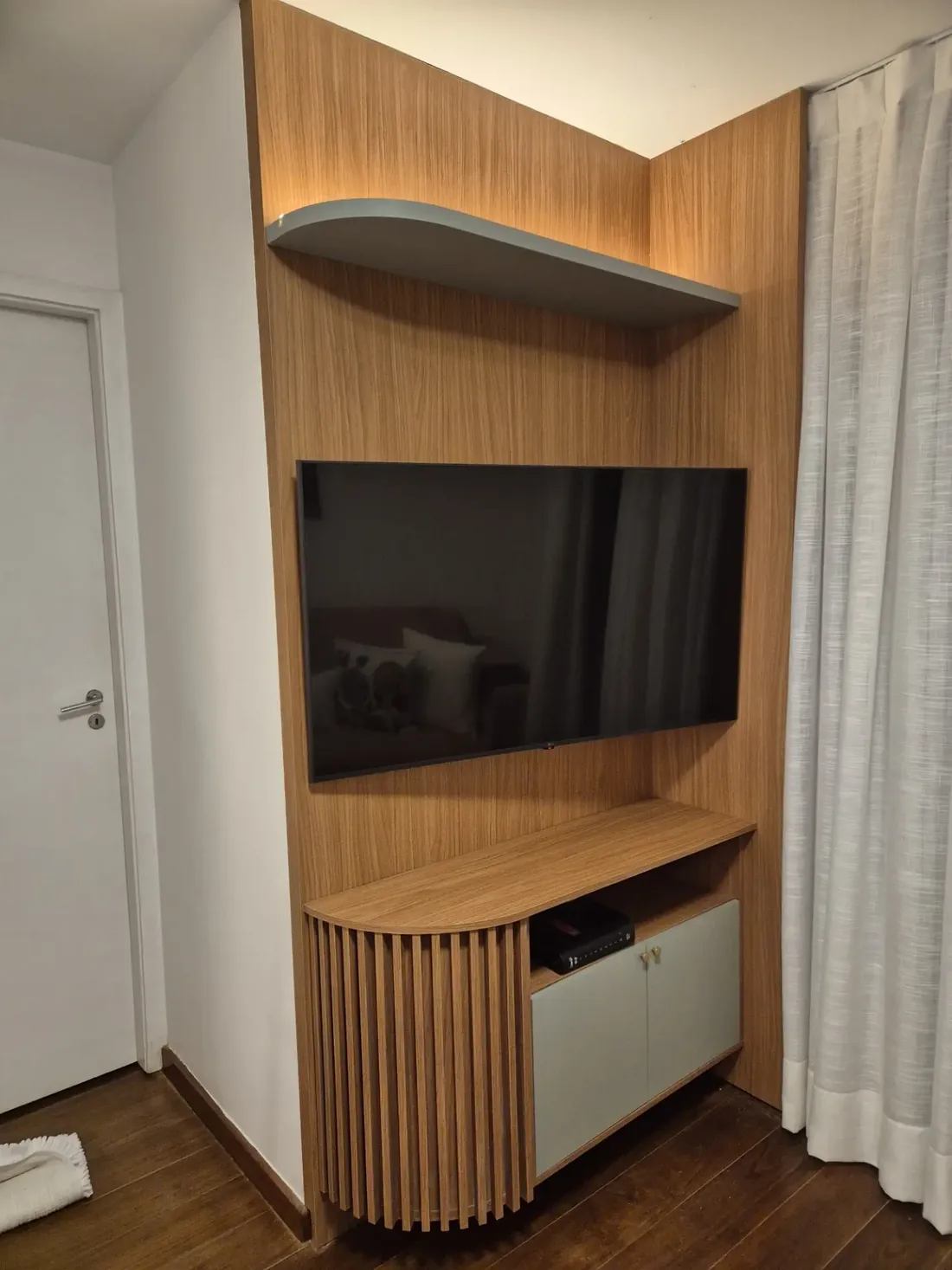 Painel de TV em madeira com prateleira curva iluminada e rack ripado na sala de estar
